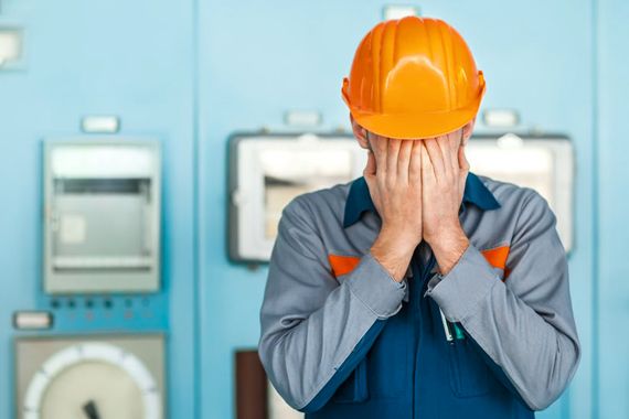 Un employé avec un casque jaune est triste devant des machines.