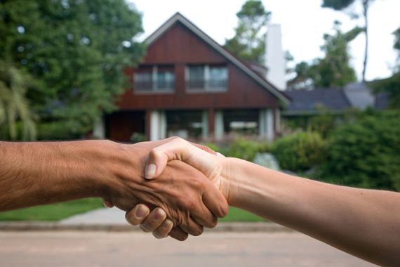 Deux personnes se serrent la main devant une maison.