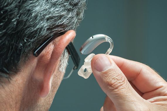 Un homme qui porte des lunettes enfile une prothèse auditive.
