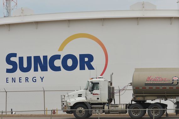 Un camion citerne roule devant un silo avec le logo de Suncor