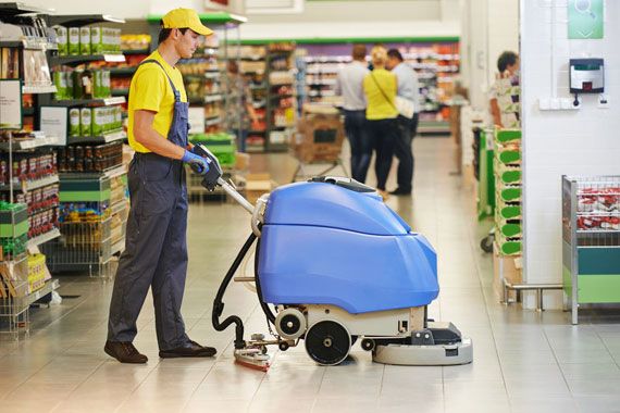 Un employé passant une polisseuse sur le plancher d'une épicerie.