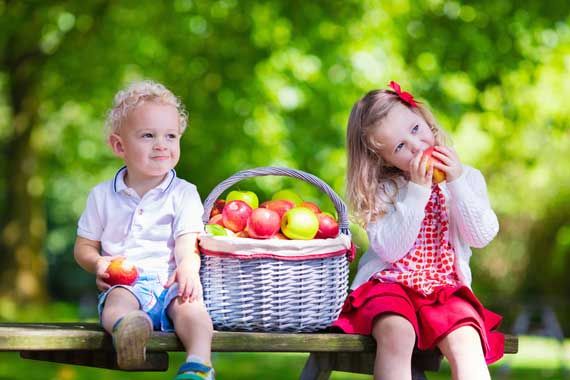 Deux enfants qui mangent chacun une pomme dans un verger.