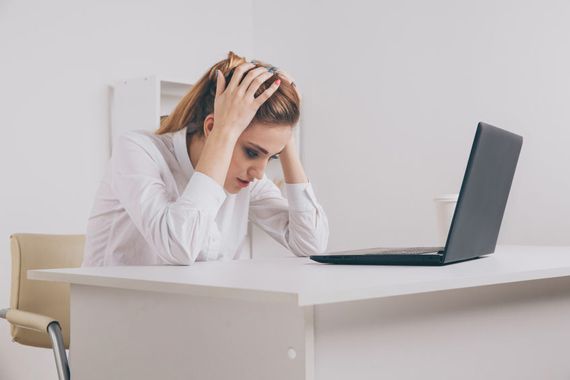 Une femme se tient la tête devant son écran d'ordinateur.
