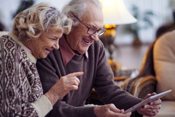 Deux grand-parents rigolent devant une tablette.