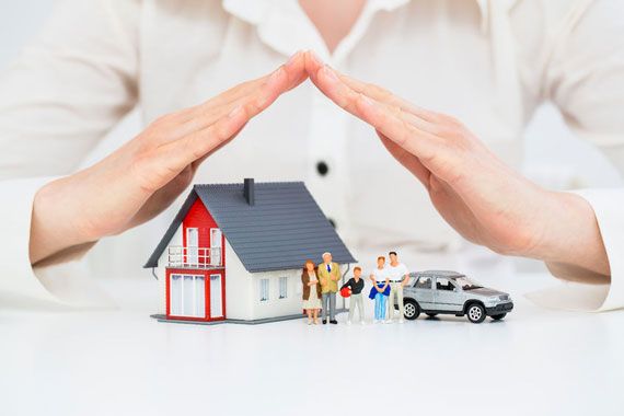 Des mains couvrent une maison, une voiture et une famille miniatures