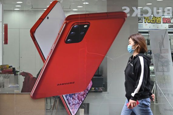 Une femme qui porte un masque chirurgical passe près d'un affiche d'un téléphone intelligent Samsung.