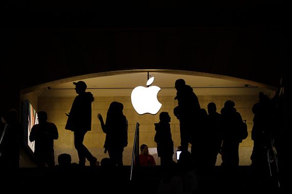 Le logo d'Apple en pancarte lumineuse devant laquelle des gens marchent.