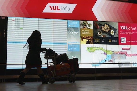 Une femme marche avec sa valise devant un écran d'information de l'aéroport Montréal-Trudeau.